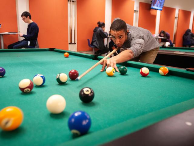 A male student lines up a pool shot on one of the MU games area tables