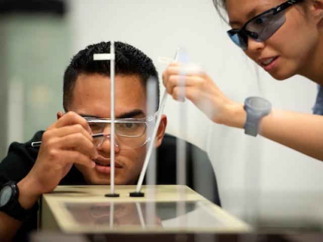 Two people in safety goggles inspect a test. 