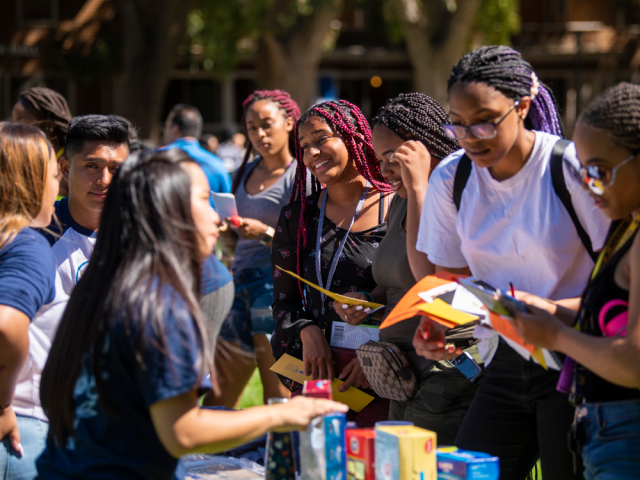 a group of students at an event talking with staff at an information table