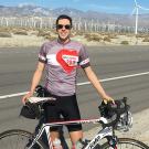 International relations graduate Tim Mizrahi poses with a road bike next to a highway with windmills in the background