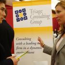 A male student listening attentively to a female representative of Triage Consulting Group at a career fair