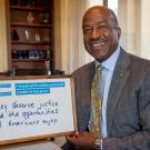 Chancellor Gary S. May, smiling, in his office, with DACA signboard.