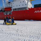 Scientist with glider and flag in front of icebreaker on top of ice