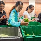 Three female students pick produce out of bins.