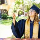 Kendal Hicks in cap and gown, waving blue and gold ribbon wands