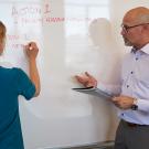 Michael Rios speaking to woman who is writing on a whiteboard.