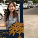 Student holds photo frame while row of cars drives past.