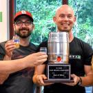 Four men holding glasses of beer and a keg trophy.