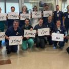 Hospital workers with signs reading "we stay here for you, please stay home for us"