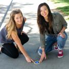 Two women glue botton down, look at camera.