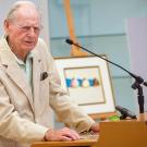 Wayne Thiebaud speaks in front of two of his paintings.