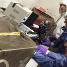 Three researchers in protective lab gloves and clothing work at lab bench