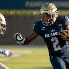 A UCC Davis football player carries the ball past a defender