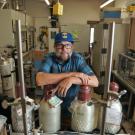 Man behind scientific equipment in lab looking at camera in blue ball cap 