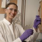 In a white lab coat and goggles, Brooke Morey works in a research lab