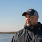 Levi Lewis in ball cap and blakc jacket with backdrop of Alviso slough in California