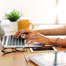 Hands typing on a laptop sitting on a wooden table