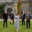 Danu artists standing on grass in front of old building.