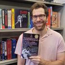 Man holds book in front of full bookshelf