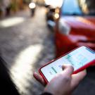 perrson holding phone with screen showing map as red car approaches 