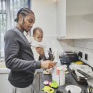 Man holding baby in his arms as he prepares infant formula. A new survey shows 81 percent of parents were forced to switch infant formulas during the May 2022 shortage, leading to undesirable health effects for babies.