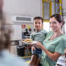 Woman holding child and plate with sandwich at lunch counter.