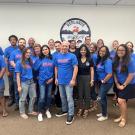 Mixed group of about 20 adults facing camera. Most are casually dressed and wearing blue sweatshirts. A logo on the wall behind them reads "Redlands Excellence in Education"