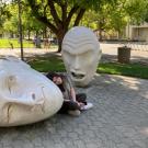 A picture of Jaimie Gelfond sitting in between the Yin & Yang Egghead sculpture.