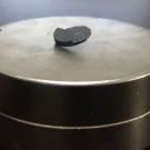 Pellet of grey stone-like material hovers in the center of a shiny metal disk. 