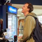 A male student looks up at a menu while the cashier waits for his order