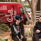 Sitting on benches, three women talk and the Health 34 van is in the background 