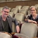 A man and a woman sitting in rows of folding seats