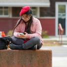 A student wearing a beret uses their smartphone outside of the UC Davis Craft Center.