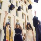 Students wearing face coverings toss their grad caps into the air.