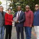 Seven people, posed in a line, with Chancellor Gary S. May and a woman holding trophy