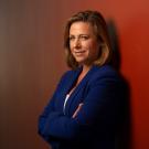 Jonna Mazet portrait, arms folded, standing against red wall