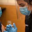 Student firefighter, in uniform, administers a vaccination.