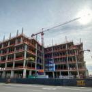 Aggie Square, a UC Davis building on the Sacramento campus, is undergoing construction. The building's framing comprised of structural beams peaks into the partially cloudy sky.