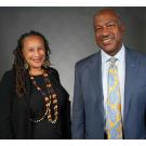 Against a black backdrop inside a recording studio, Professor Beth Rose Middleton, standing on the left, is next to Chancellor Gary S. May.