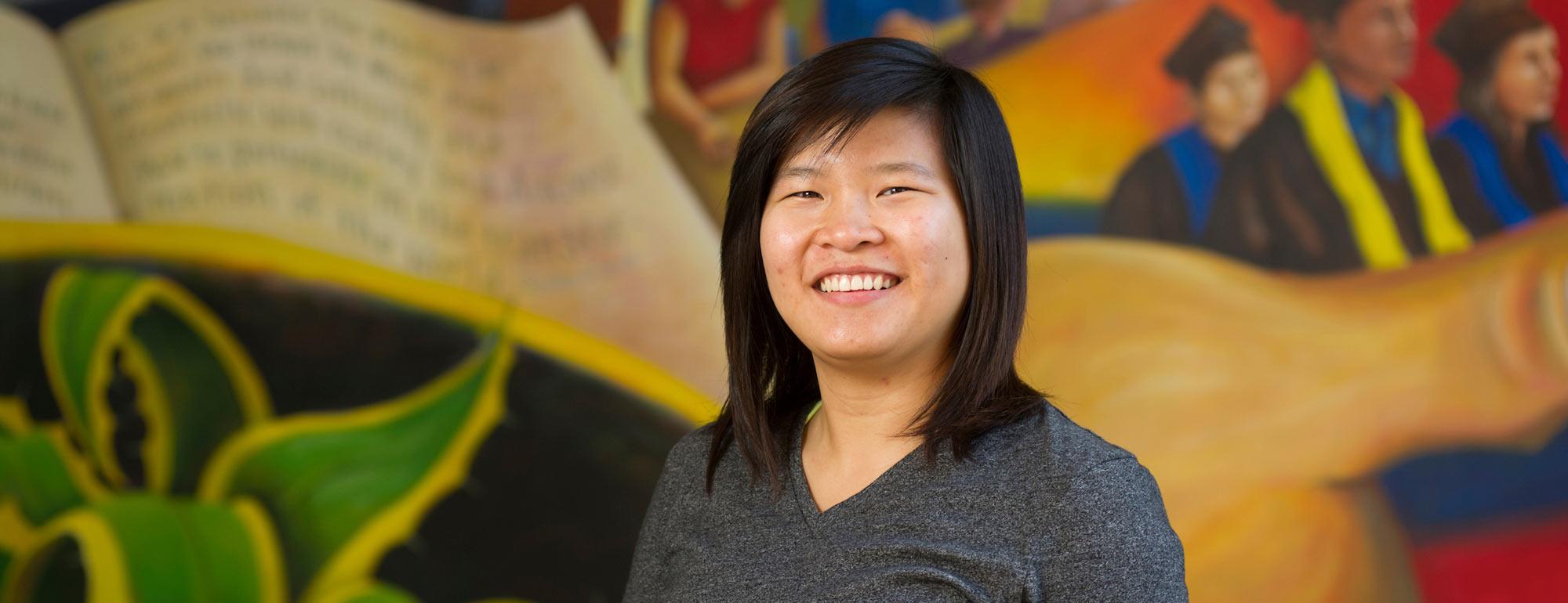 A female student poses in front of a mural 