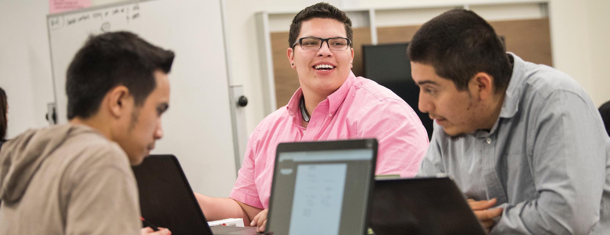 Three males students in a lively discussion over their laptops