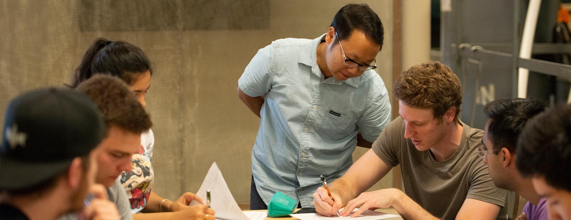 A teaching assistant leans over to assist a student during an engineering class.