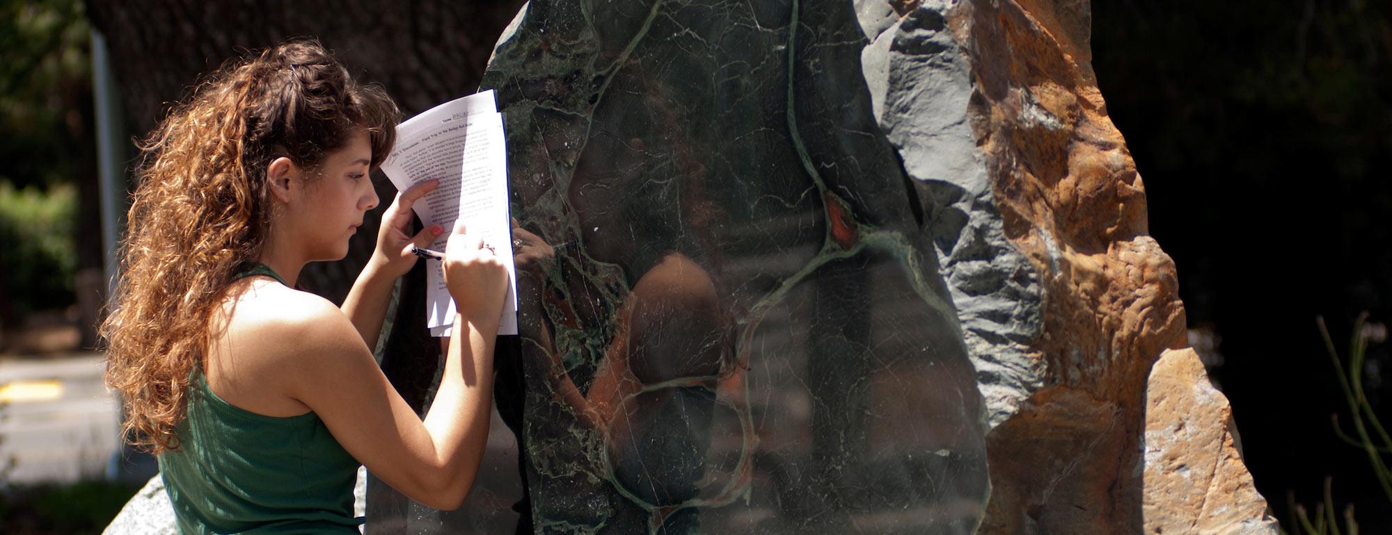 A female student takes notes about a rock present on the UC Davis campus