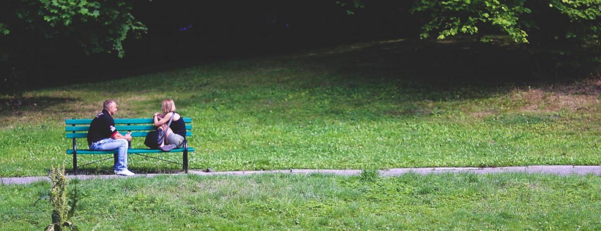 two people talking on a bench in a park