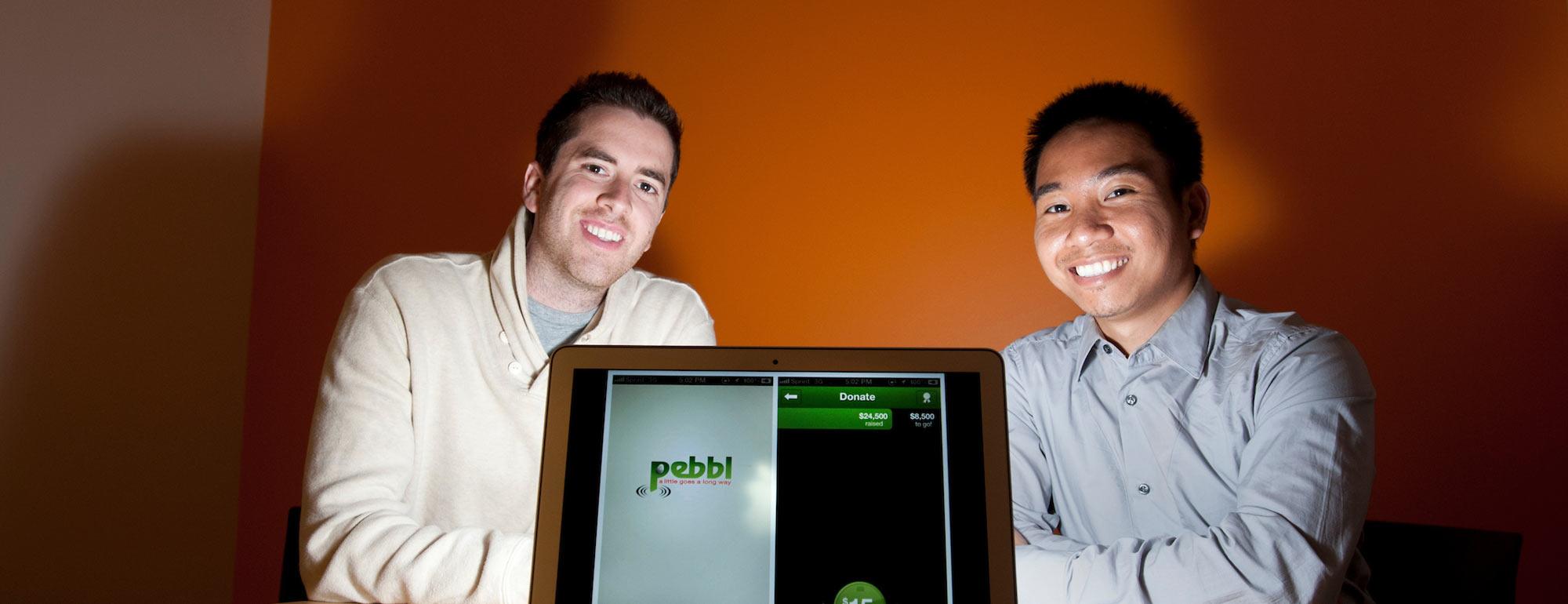 Two Graduate students pose with a laptop that shows the app that they created.