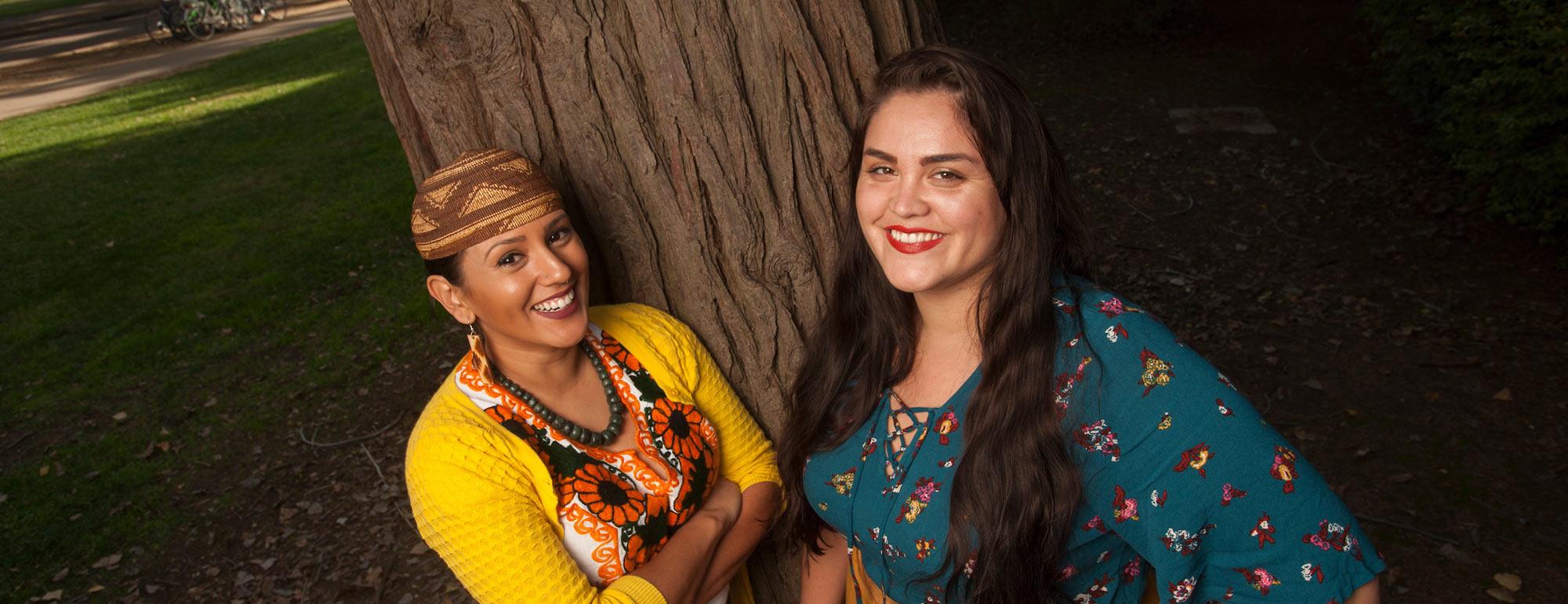 Two women pose in front of one of the oak trees on the UC Davis campus