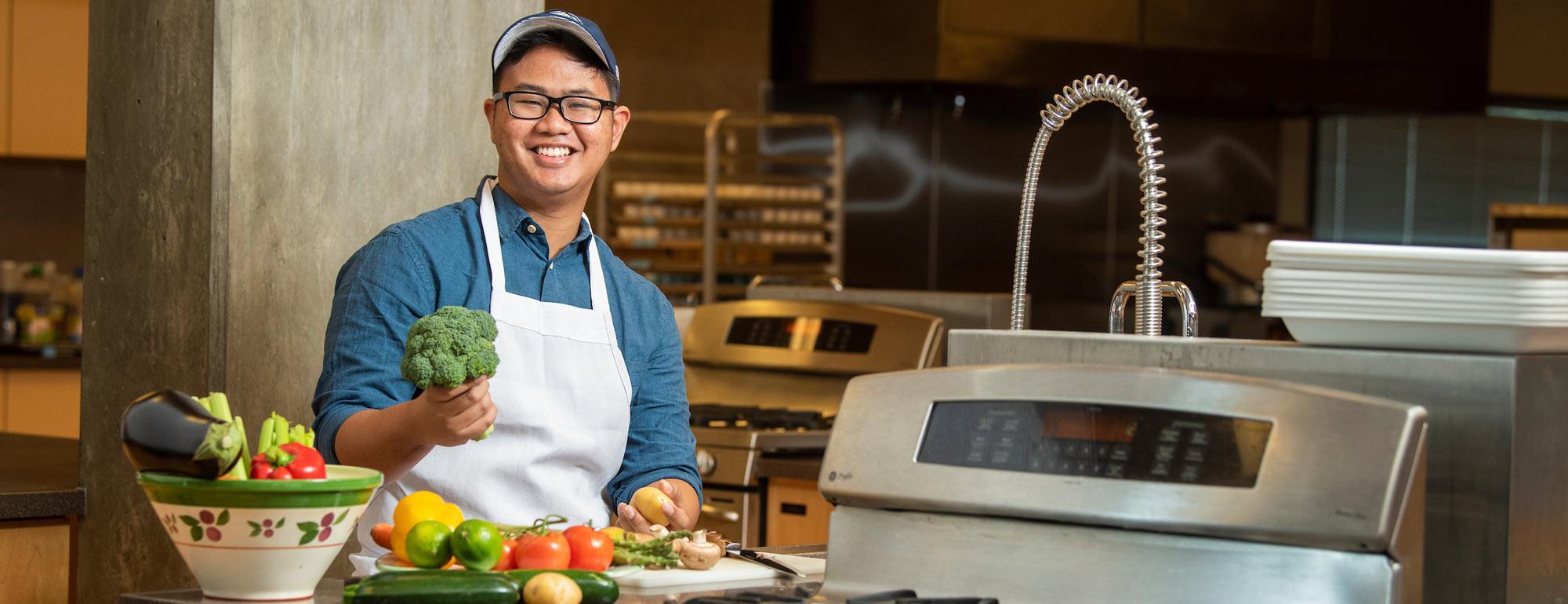 A male student poses with fruits and veggies in the research kitchen