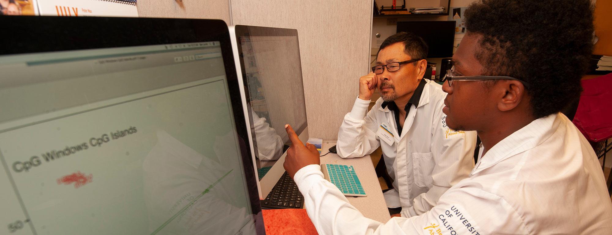 A student and professor review lab results on two large computer monitors