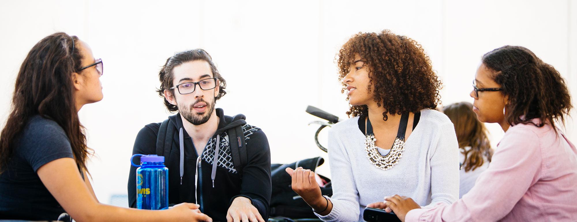 a group of four students sitting around a table discussing something