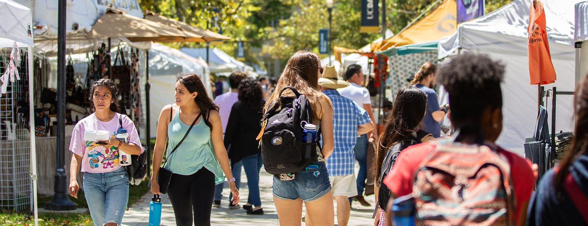 students walking down a row of vendor tents during an event on the quad